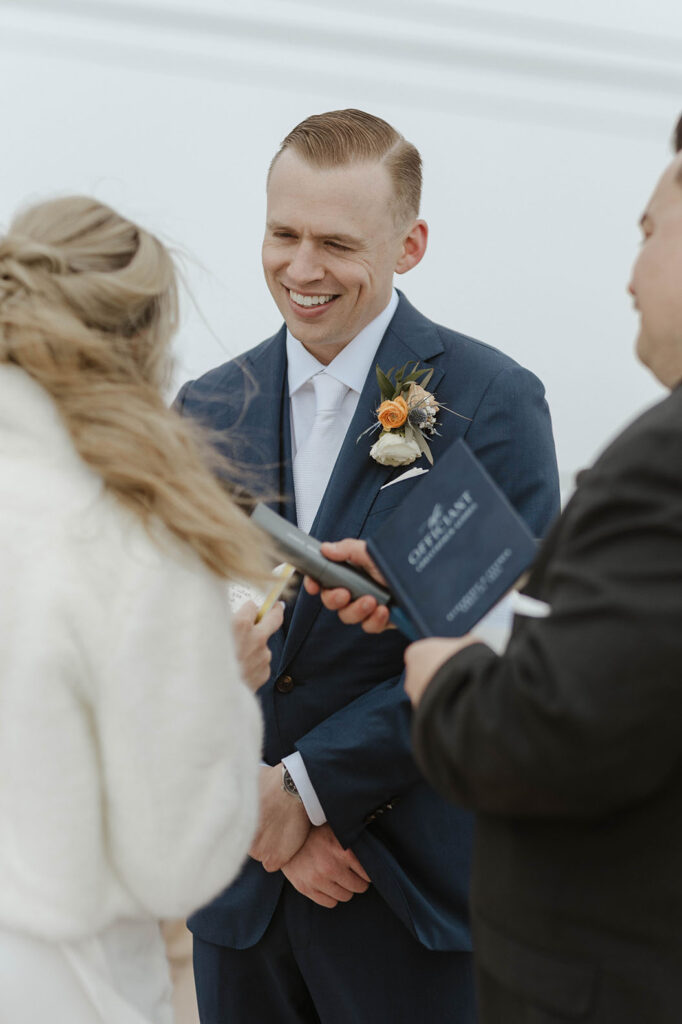Groom smiling at bride while she reads wedding vows during ceremony at Palisades Tahoe