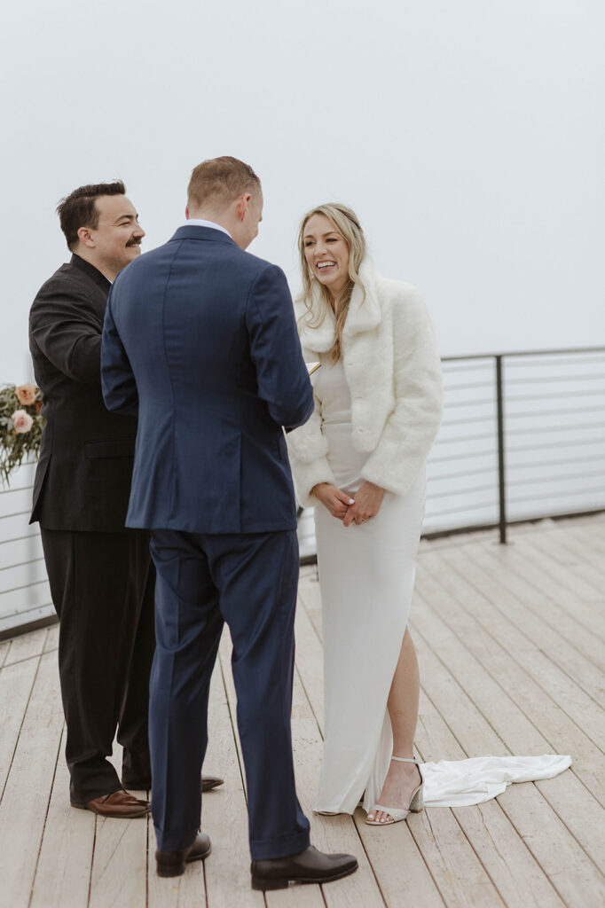 Bride smiling while groom is reading wedding vows during ceremony on overlook at Palisades Tahoe