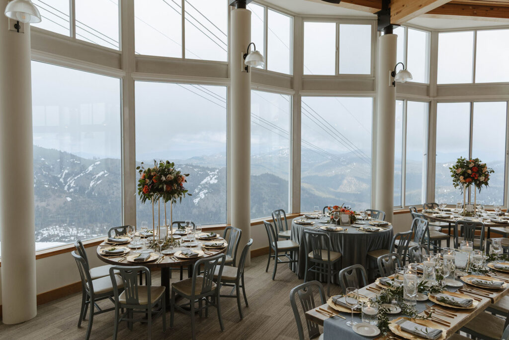 Wedding reception tables with gray and gold theme and floral decor and large windows at Palisades Tahoe