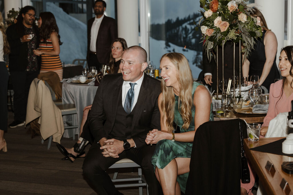 Wedding guests laughing while sitting during reception at Palisades Tahoe