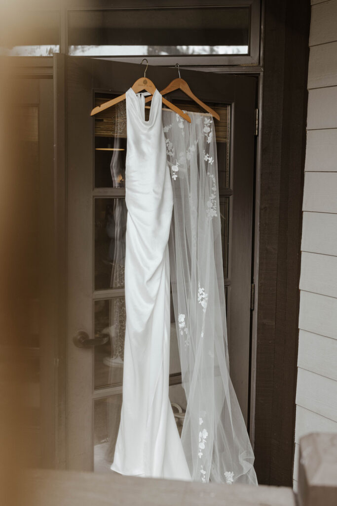 Wedding dress hanging on wooden hanger on dark brown door