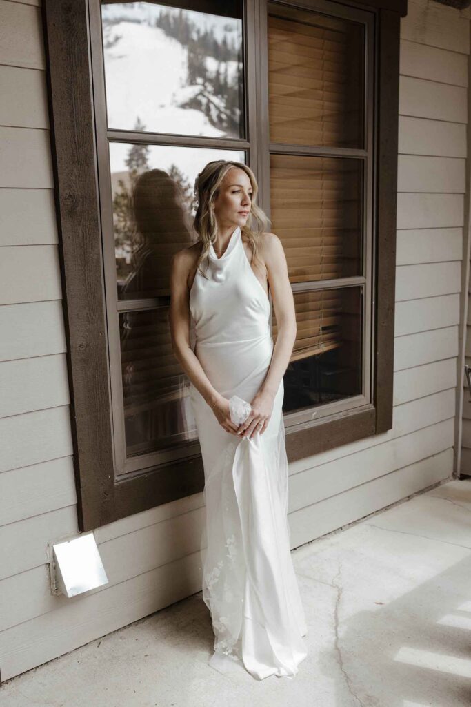 Bride holding wedding dress while standing on patio at Palisades Tahoe and looking into distance
