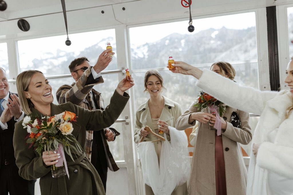 Wedding bride and guests holding up drinks while inside tram car at Palisades Tahoe with mountains in background