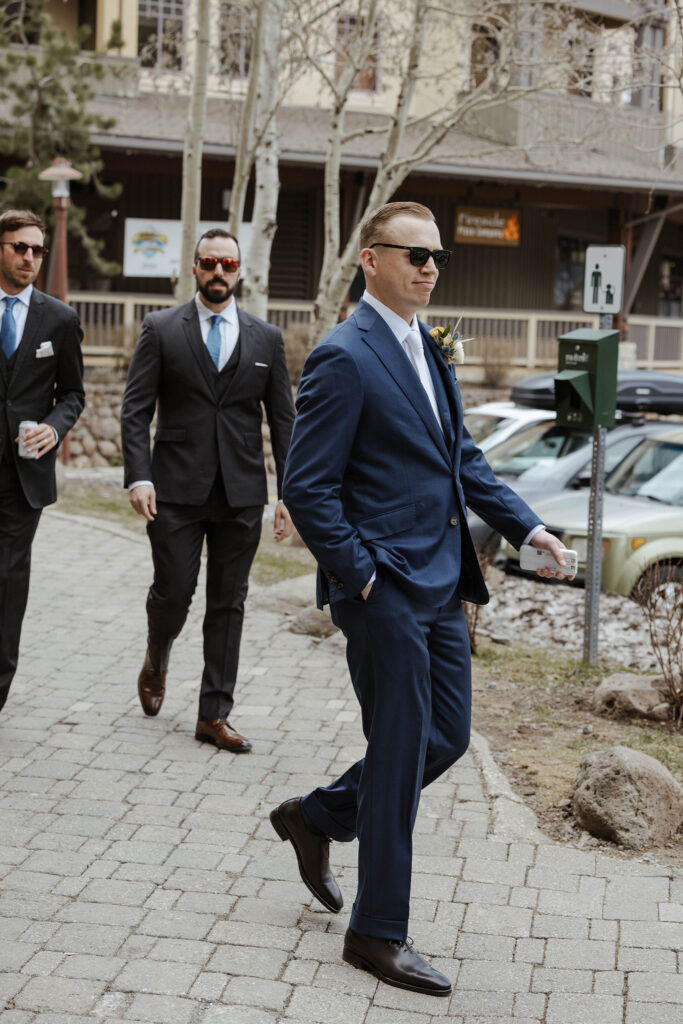 Groom walking along brick pathway with hand in pocket and groomsmen walking behind him at Palisades Tahoe