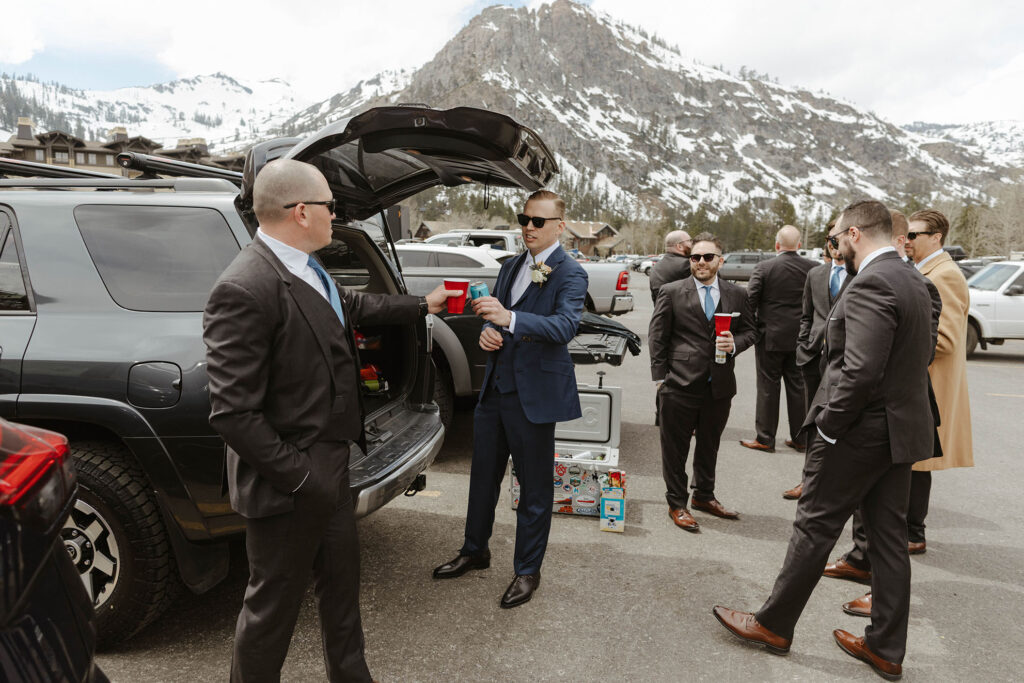 Groom cheering drinks with groomsman while hanging out and drinking in parking lot at Palisades Tahoe