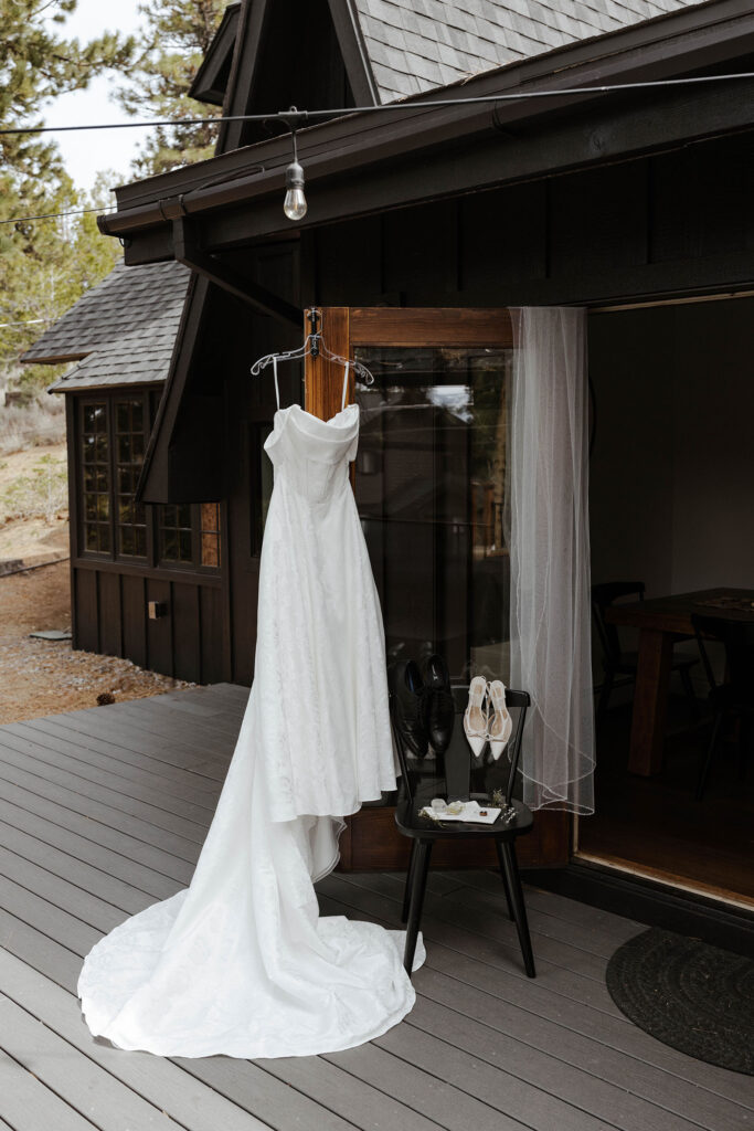 Wedding dress hanging on wooden door next to shoes and details on metal chair in South Lake Tahoe