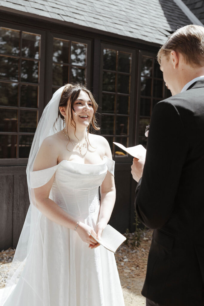 Bride smiling while groom reads wedding vows to her during first look in South Lake Tahoe