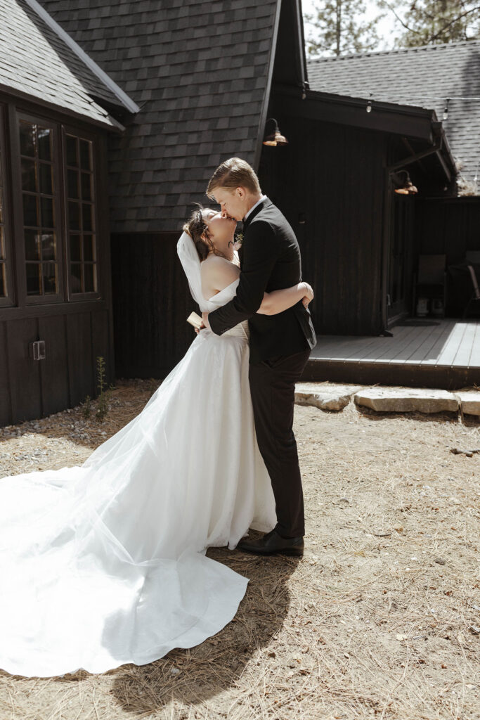 Wedding couple holding each other while kissing in front of dark wooden buildings in South Lake Tahoe