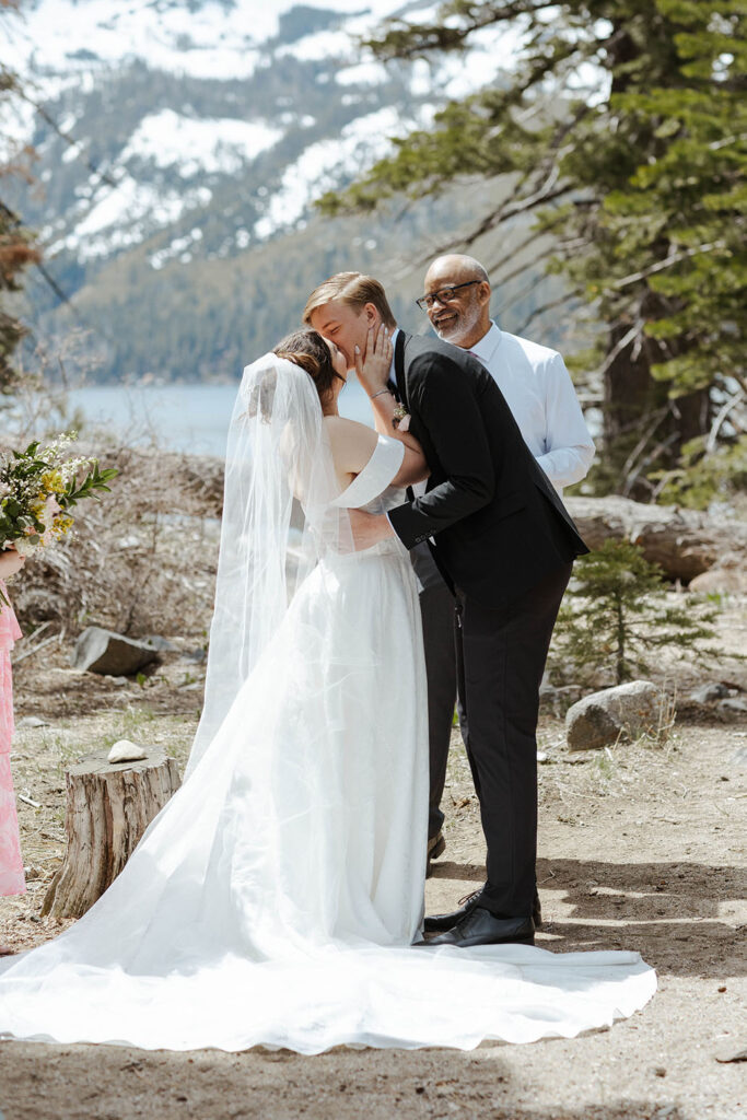 Wedding couples first kiss after ceremony in South Lake Tahoe with pine trees and snowy mountains in background