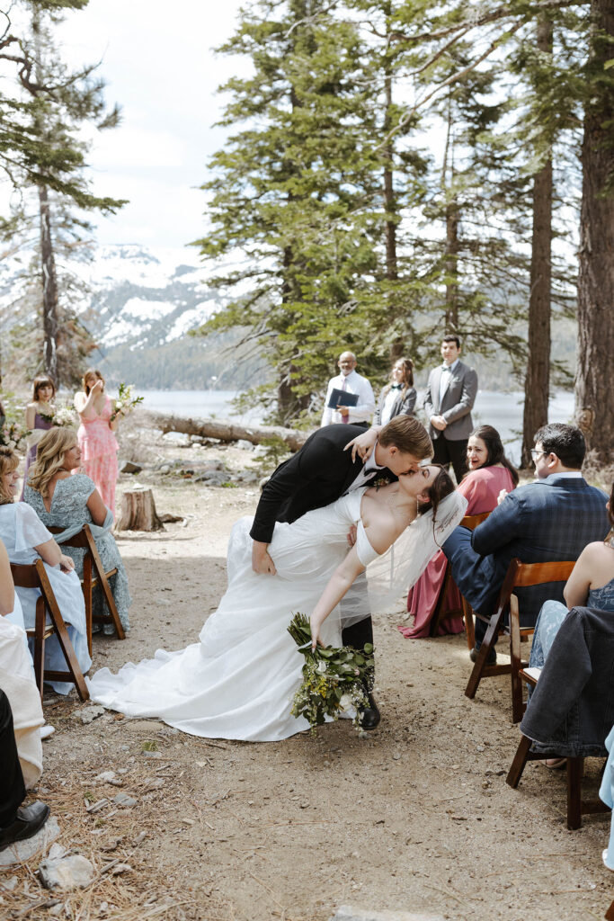 Groom leaning bride back and kissing her in the wedding aisle after ceremony in South Lake Tahoe with guests clapping