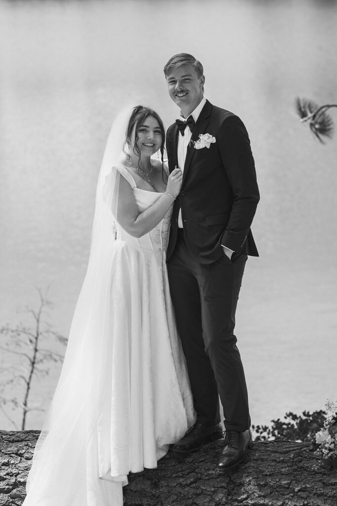 Wedding couple holding each other while standing on a log and smiling at camera with Lake Tahoe behind them
