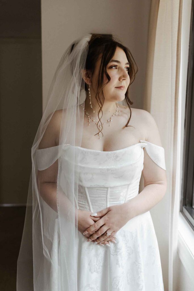 Bride in wedding dress looking to the side out of window with hands folded in front of her in South Lake Tahoe