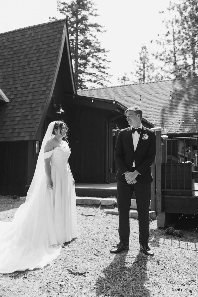 Groom smiling while turning around to see bride in wedding dress during first look in front of wooden buildings in South Lake Tahoe