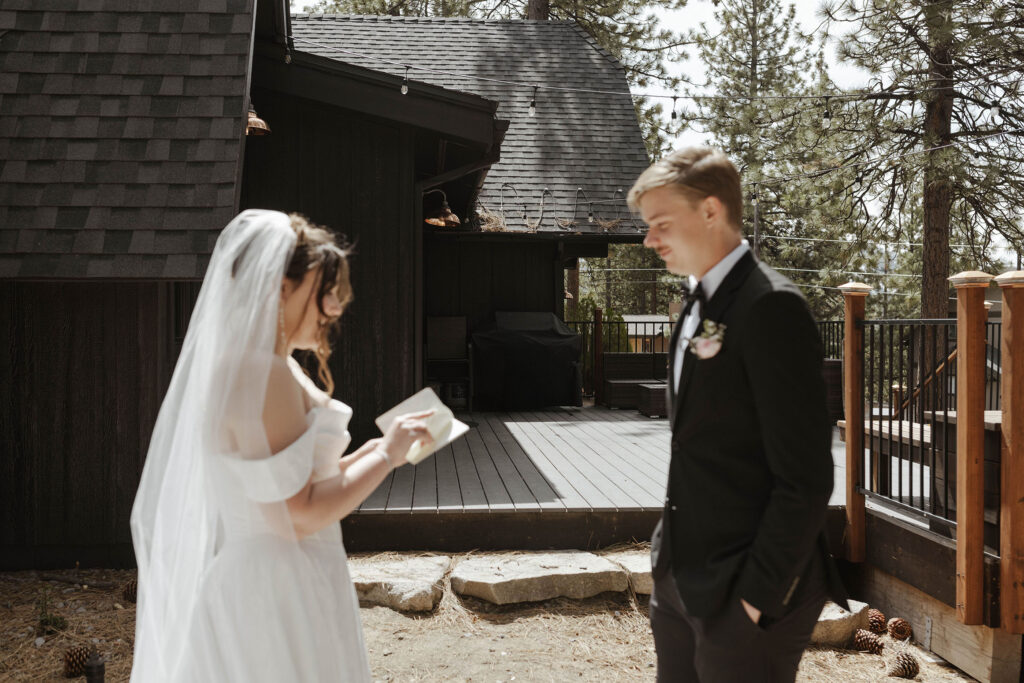 Bride reading wedding vows to groom in front of dark wooden buildings and pine trees in South Lake Tahoe