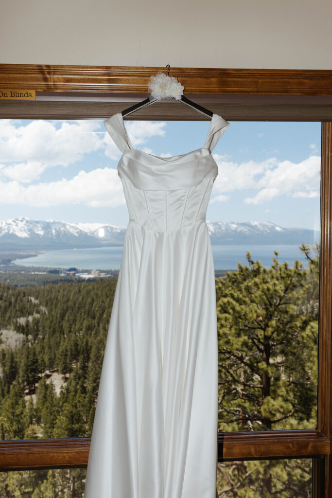 white wedding dress with sleeves hanging from a window overlooking lake tahoe at tahoe blue estate