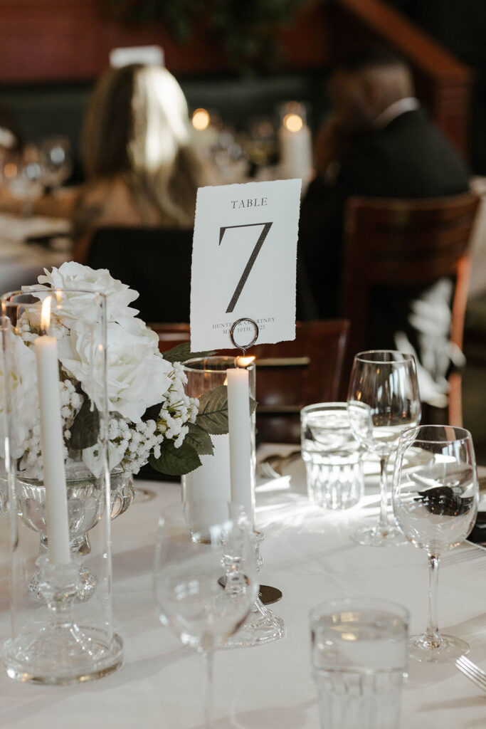 table 7 signage with white candles and glassware at a wedding reception at riva grill