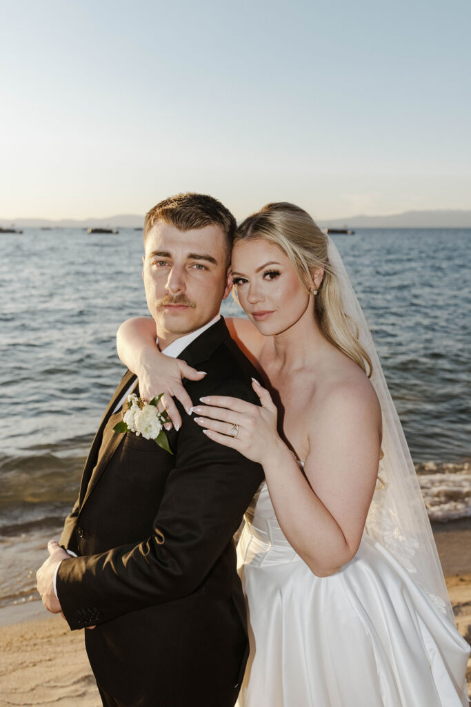 bride hugging groom from behind and both are looking at the camera at sunset at riva grill