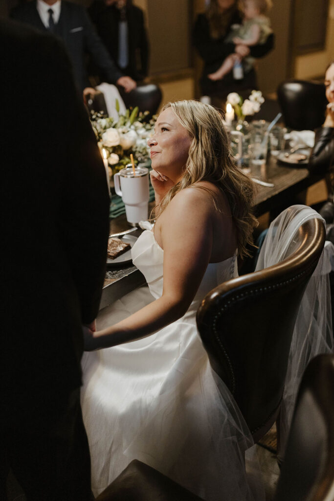 bride looking at her husband, holding his hand while he gives a speech at the dinner table