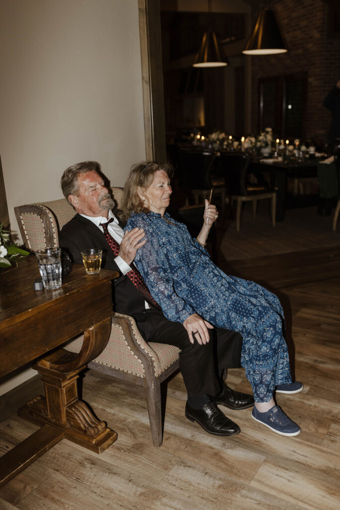 grandparents sitting on each others lap watching the newlyweds share a first dance