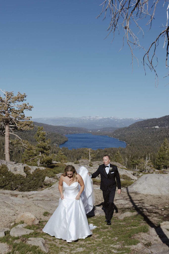 bride walking while groom holds her dress train with donner lake in the distance