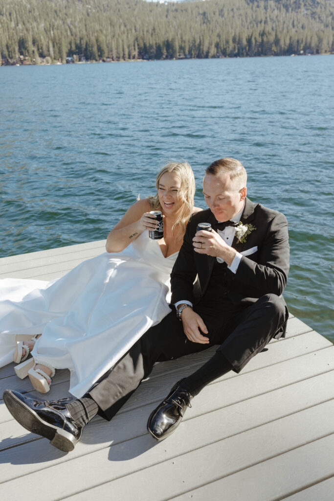 couple sitting on a dock at donner lake for their elopement while laughing and holding beers