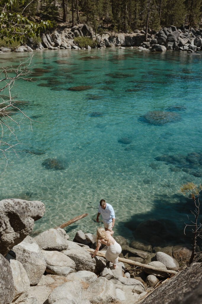 Groom helping bride down large rocks to the water at Emerald Bay in Lake Tahoe