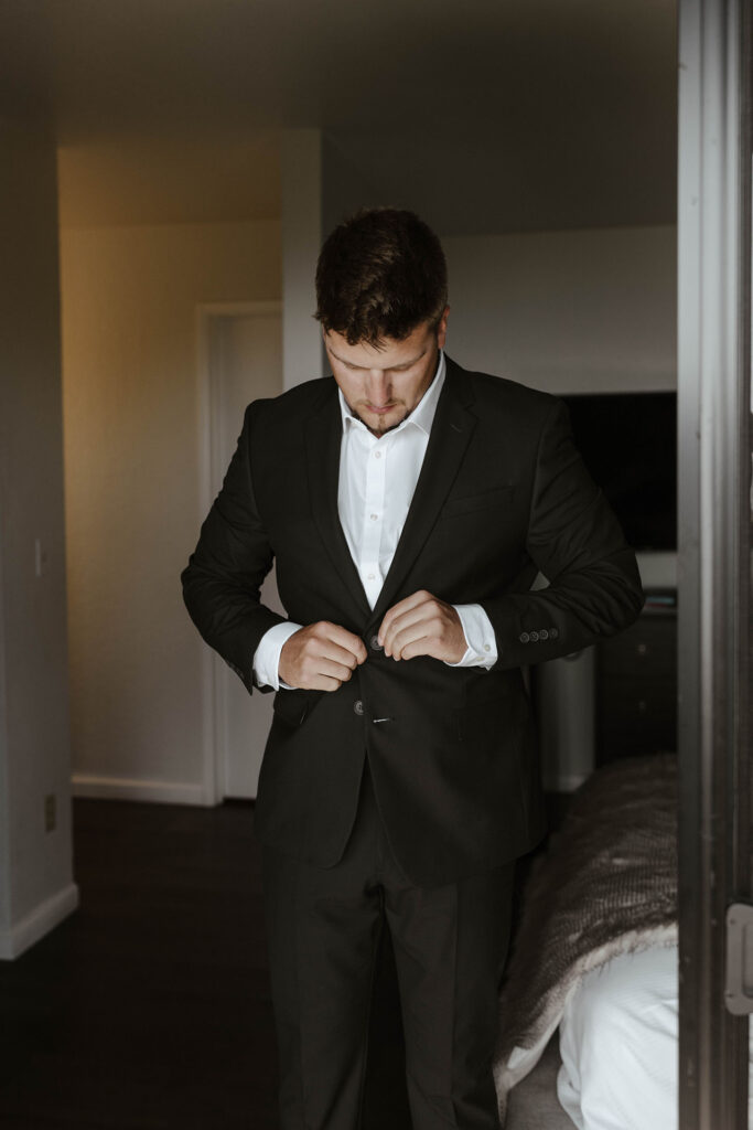 Groom looking down and buttoning black suit jacket