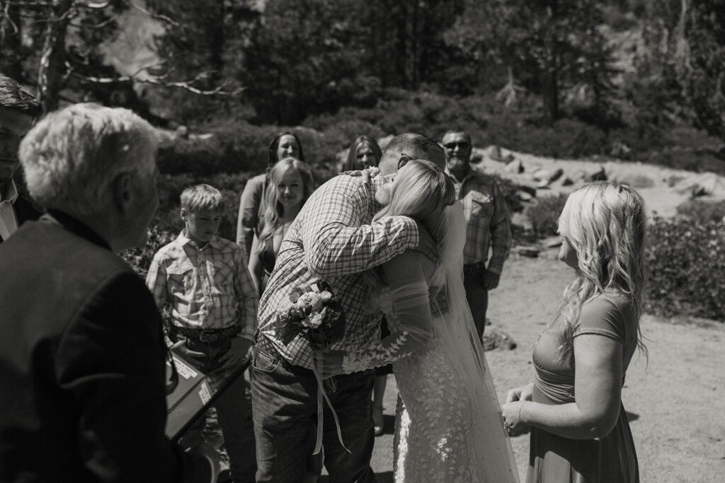 Bride's dad hugging bride during Elopement ceremony at Emerald Bay with guests in background