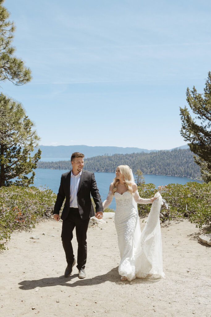 Elopement couple holding hands while smiling at each other and walking up dirt path together at Emerald Bay