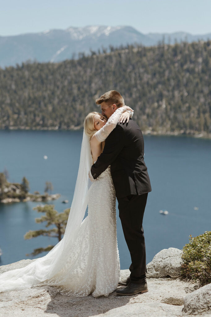 Elopement couple hugging while standing on rocky ledge together at Emerald Bay with Lake Tahoe in background