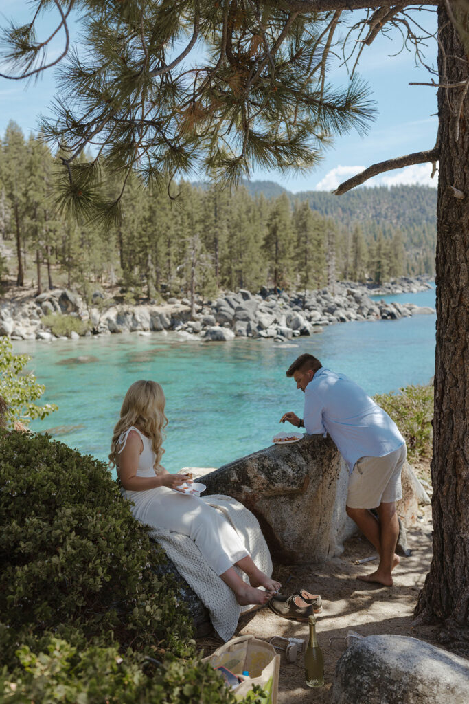 Elopement couple leaning on rocks eating pizza together while at Emerald Bay with Lake Tahoe in background