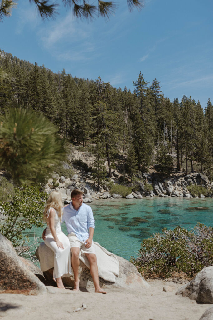 Elopement couple sitting on rock together at Emerald Bay with Lake Tahoe and pine trees in background