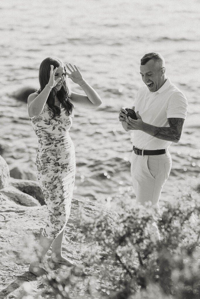 black and white photo of man excited smiling holding ring box and woman excited and laughing after proposing