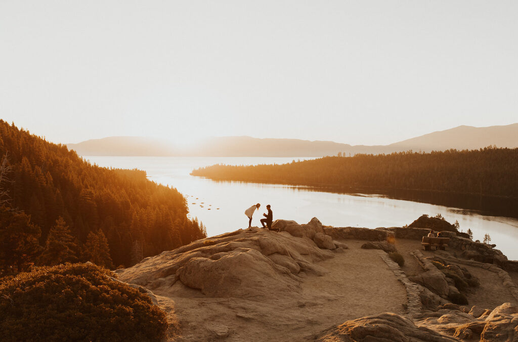 man on one knee proposing to a woman bent over in shock at sunrise at emerald bay in lake tahoe