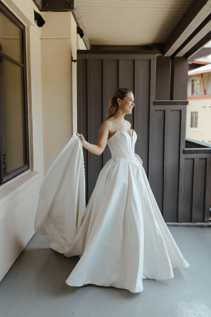 Bride holding back of wedding dress while smiling and standing outside on patio at Palisades Tahoe