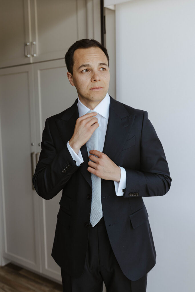 Wedding groom adjusting tie while looking off to the side at Palisades Tahoe