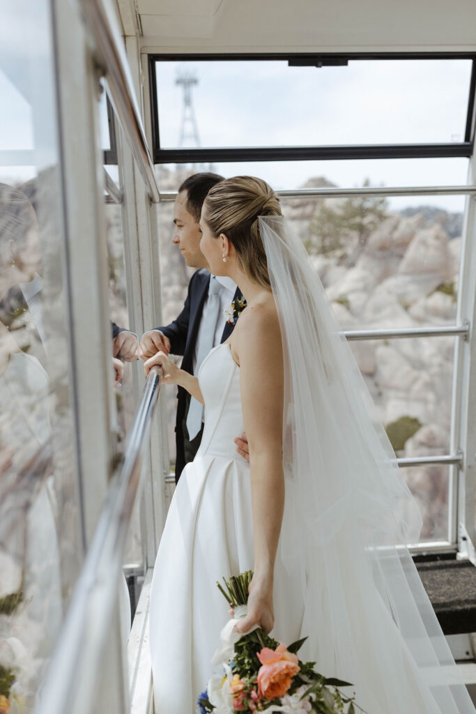 Wedding couple holding railing and looking out window of tram while riding up to High Camp at Palisades Tahoe