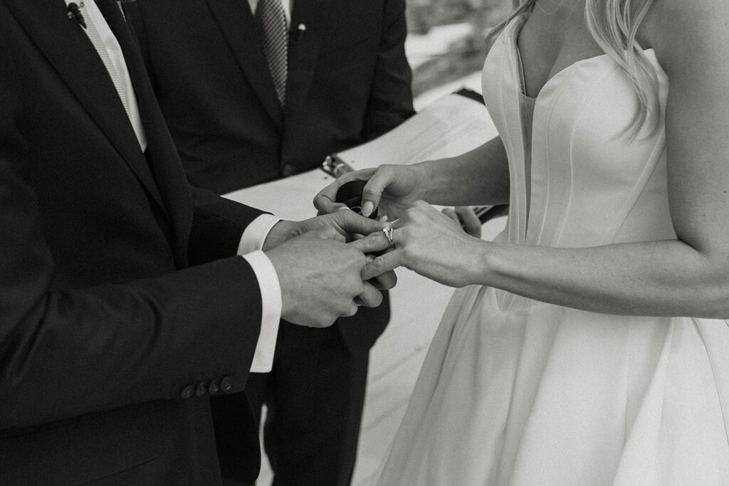 Groom sliding wedding ring onto bride's finger during ceremony at High Camp