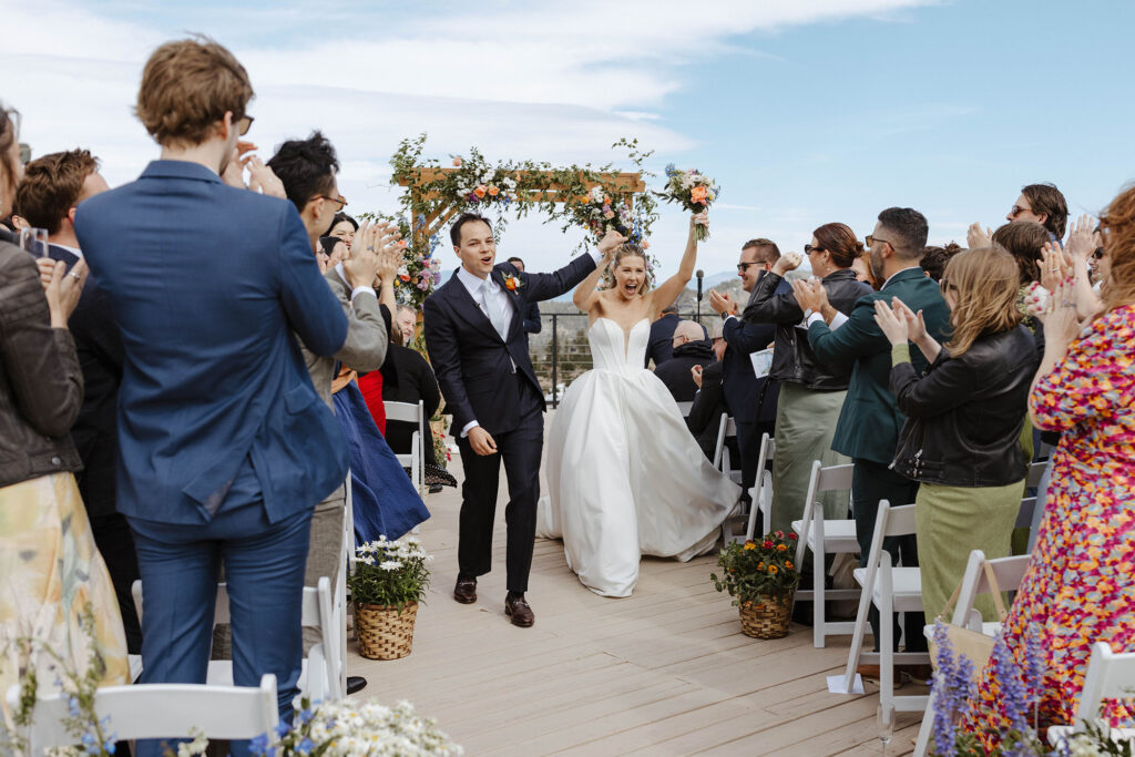 Wedding couple celebrating and holding hands in air together while walking down aisle and guests clap after ceremony at High camp