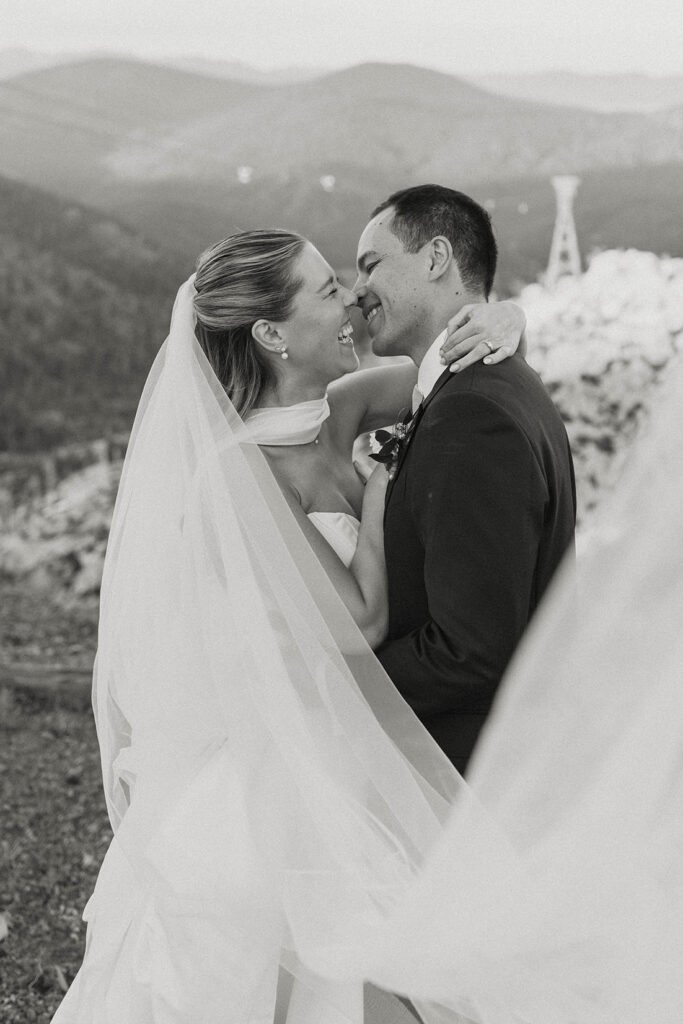 Wedding couple laughing while their faces almost touch and veil partially covers camera lens at High Camp with mountains in background