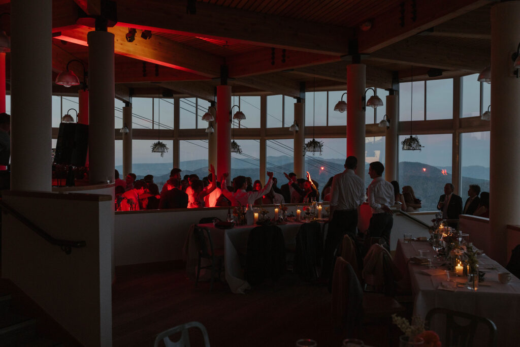 Wedding reception at High Camp with guests dancing and celebrating and mountains visible through windows