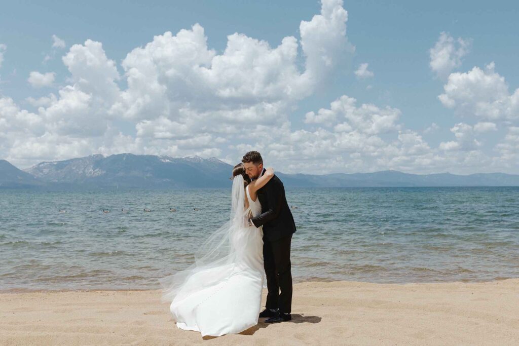 Elopement couple hugging on sandy beach in Emerald Bay with Lake Tahoe and mountains in background