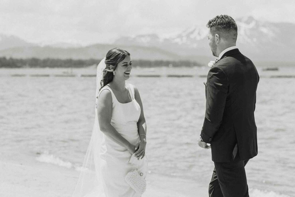 Elopement bide smiling at groom while on sandy beach in Emerald Bay with Lake Tahoe and mountains in background