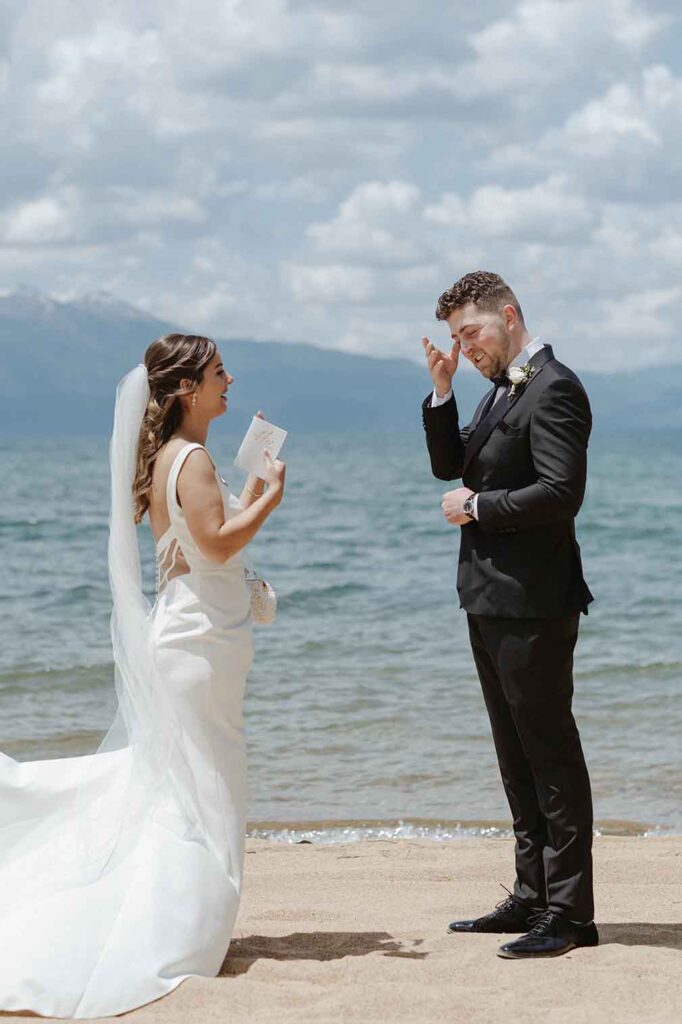 Elopement groom emotional while bride reads wedding vows to him and standing on a sandy beach at Emerald Bay in Lake Tahoe