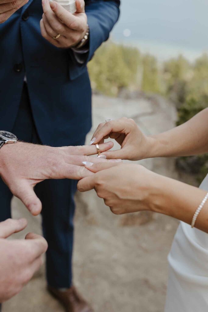 Close up of bride sliding wedding ring onto groom's finger during elopement ceremony at Emerald Bay