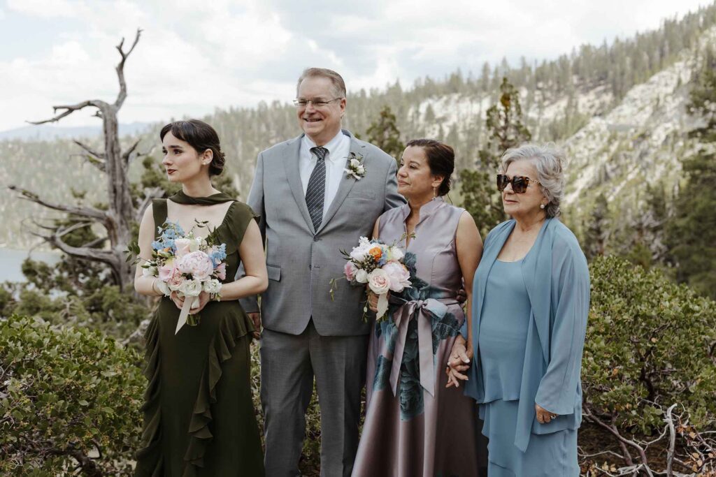 Family watching elopement ceremony at Emerald Bay with pine trees in background