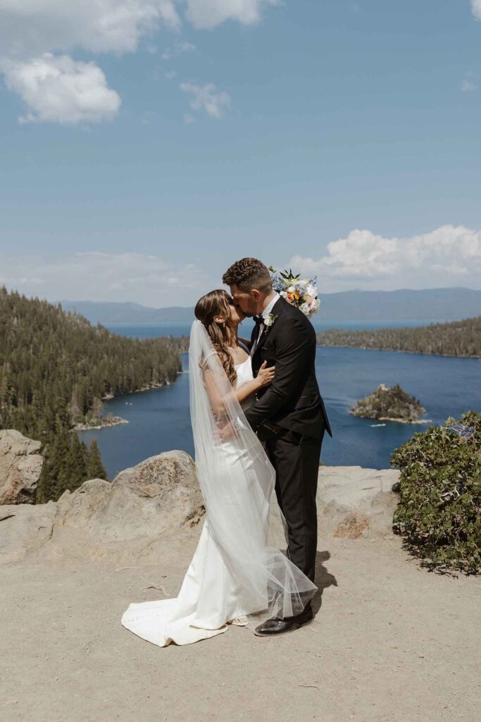 Elopement couple holding each other and kissing overlooking Emerald Bay and lots of pine trees