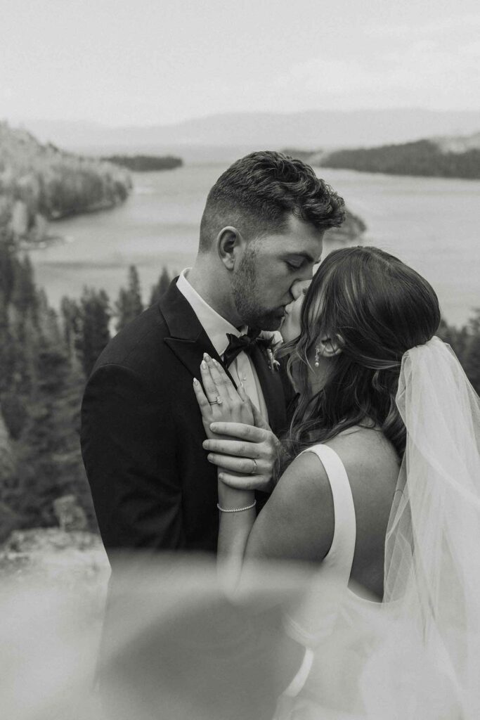 Elopement couple kissing while bride's veil blows partially in front of camera at Emerald Bay with Lake Tahoe in background