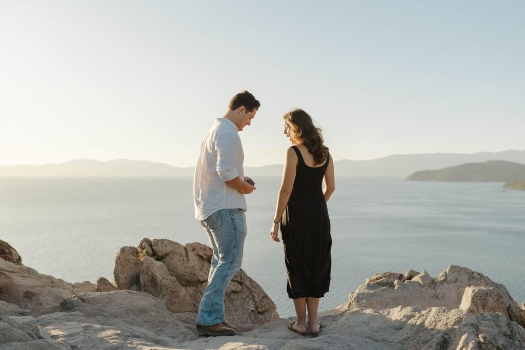 Woman surprised looking at man pulling out ring box while standing atop Eagle Rock in Lake Tahoe