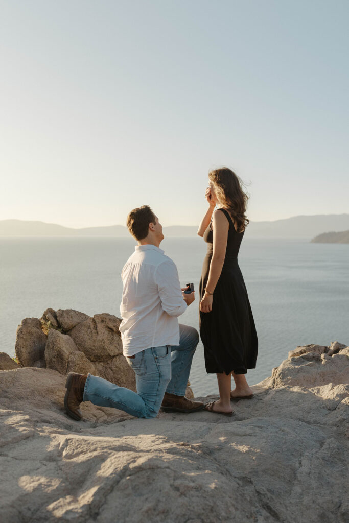 Man on one knee holding ring and proposing while atop Eagle Rock in Lake Tahoe